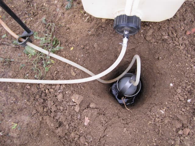 Essai Porchet en cours — bidon d'eau alimentant un cylindre de mesure planté dans une fosse